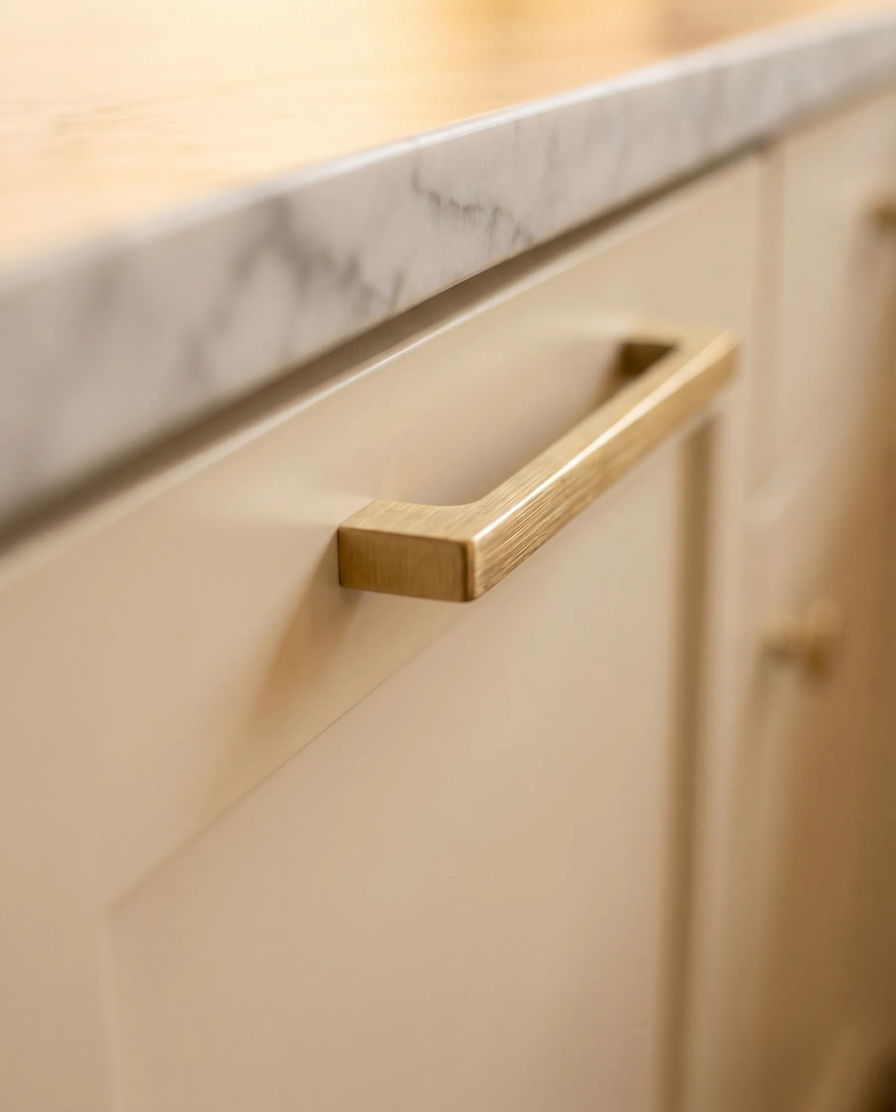 Brushed brass cabinet hardware on warm white shaker cabinets with a honed marble counter edge