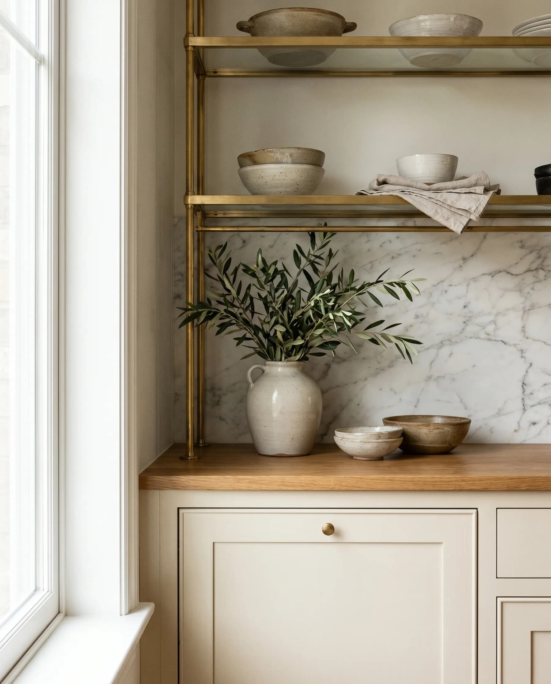A styled kitchen design detail with brass open shelving and a marble backsplash